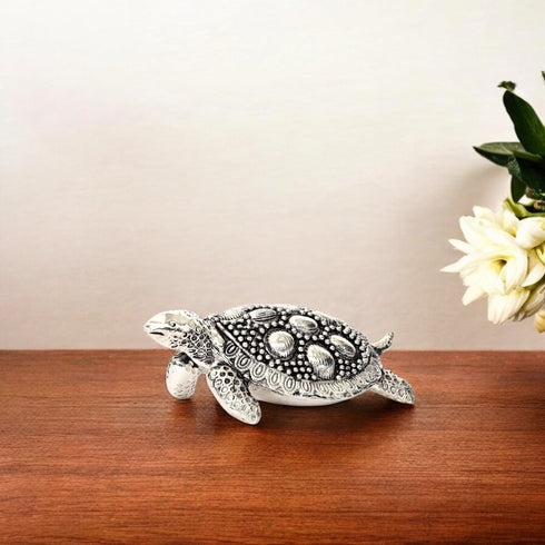 A handcrafted German silver turtle decor placed on a wooden surface, with intricate circular patterns on its shell and a polished silver body.