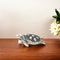 A handcrafted German silver turtle decor placed on a wooden surface, with intricate circular patterns on its shell and a polished silver body.