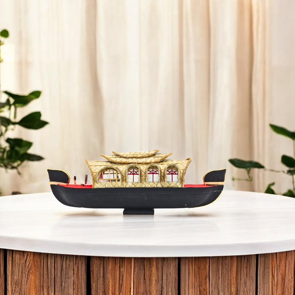 A miniature model of a Kerala house boat with a woven palm leaf canopy, featuring a black and gold color scheme, displayed on a wooden surface.