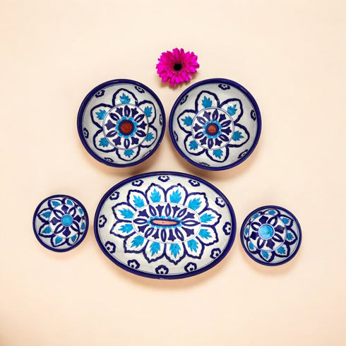 A set of handcrafted blue and white floral patterned ceramic dishes, including five pieces displayed on a neutral background with a pink flower.