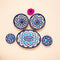 A set of handcrafted blue and white floral patterned ceramic dishes, including five pieces displayed on a neutral background with a pink flower.