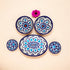 A set of handcrafted blue and white floral patterned ceramic dishes, including five pieces displayed on a neutral background with a pink flower.