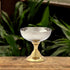 A two-tone ceremonial chalice with a silver-finish basin on a brass pedestal, displayed on a wooden surface with foliage in the background.