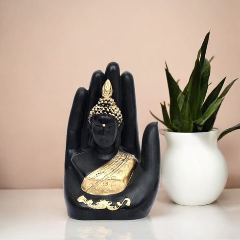 Black and gold Buddha statue in a hand shape with a white vase and plant in the background.
