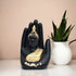 Black and gold Buddha statue in a hand shape with a white vase and plant in the background.