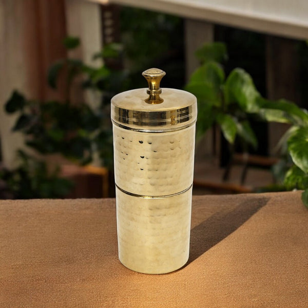 Brass pepper grinder on a wooden surface with a blurred indoor background