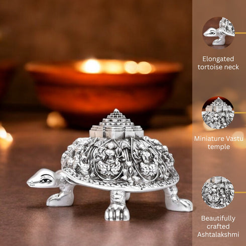Decorative silver turtle with miniature temple on a wooden surface, lit candle in the background