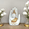 Decorative statue of a Buddha figure in a hand with white flowers on a wooden surface.
