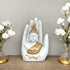 Decorative statue of a Buddha figure in a hand with white flowers on a wooden surface.