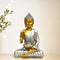 Gold and silver Buddha statue with a blurred plant on a beige background
