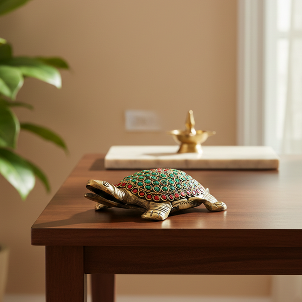 Decorative turtle figurine with colored stones on a wooden table, with a plant and wall socket in the background.