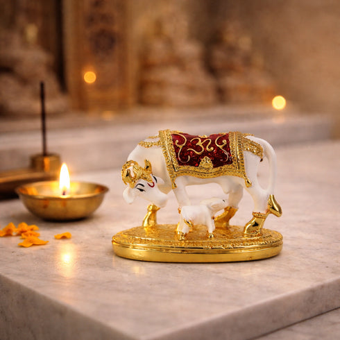Decorative statue of a cow and calf with gold accents on a marble surface, with a lit candle in the background.