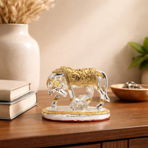 Decorative statue of a bull with two calves on a wooden surface, with books and a vase in the background.