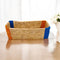 A handwoven Sabai Grass storage organizer with beige body and blue and orange trim, placed on a table with a floral arrangement in the background.
