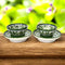 Handcrafted Blue Pottery bowl and plate set with floral motifs on a green and white background, placed on a wooden surface with foliage in the background.
