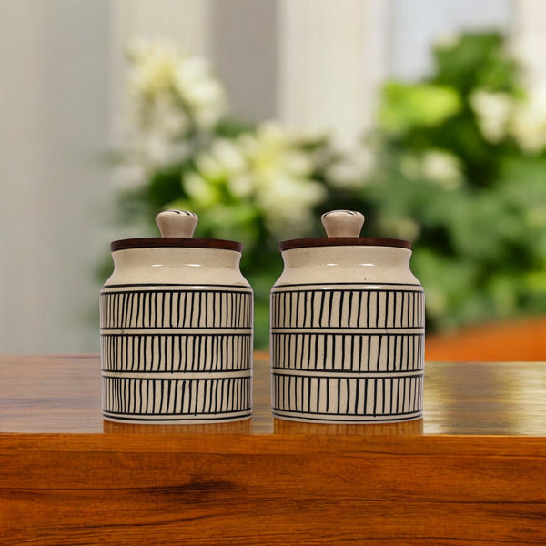 Two ceramic jars with black horizontal and vertical lines pattern, displayed on a wooden surface with a blurred background.