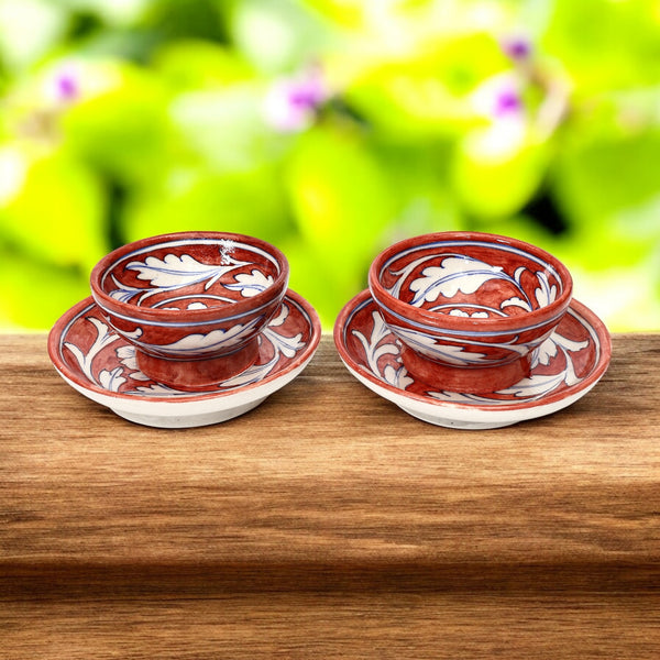 Two handcrafted red floral decorative bowls on a wooden surface with a blurred green background.