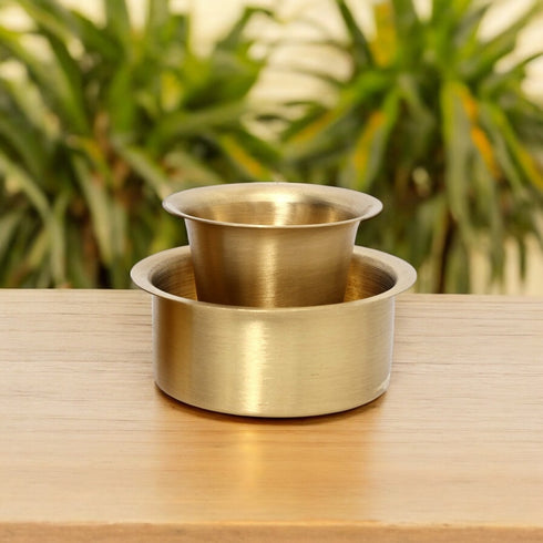 Two metallic bowls stacked on a wooden surface with a blurred green plant background