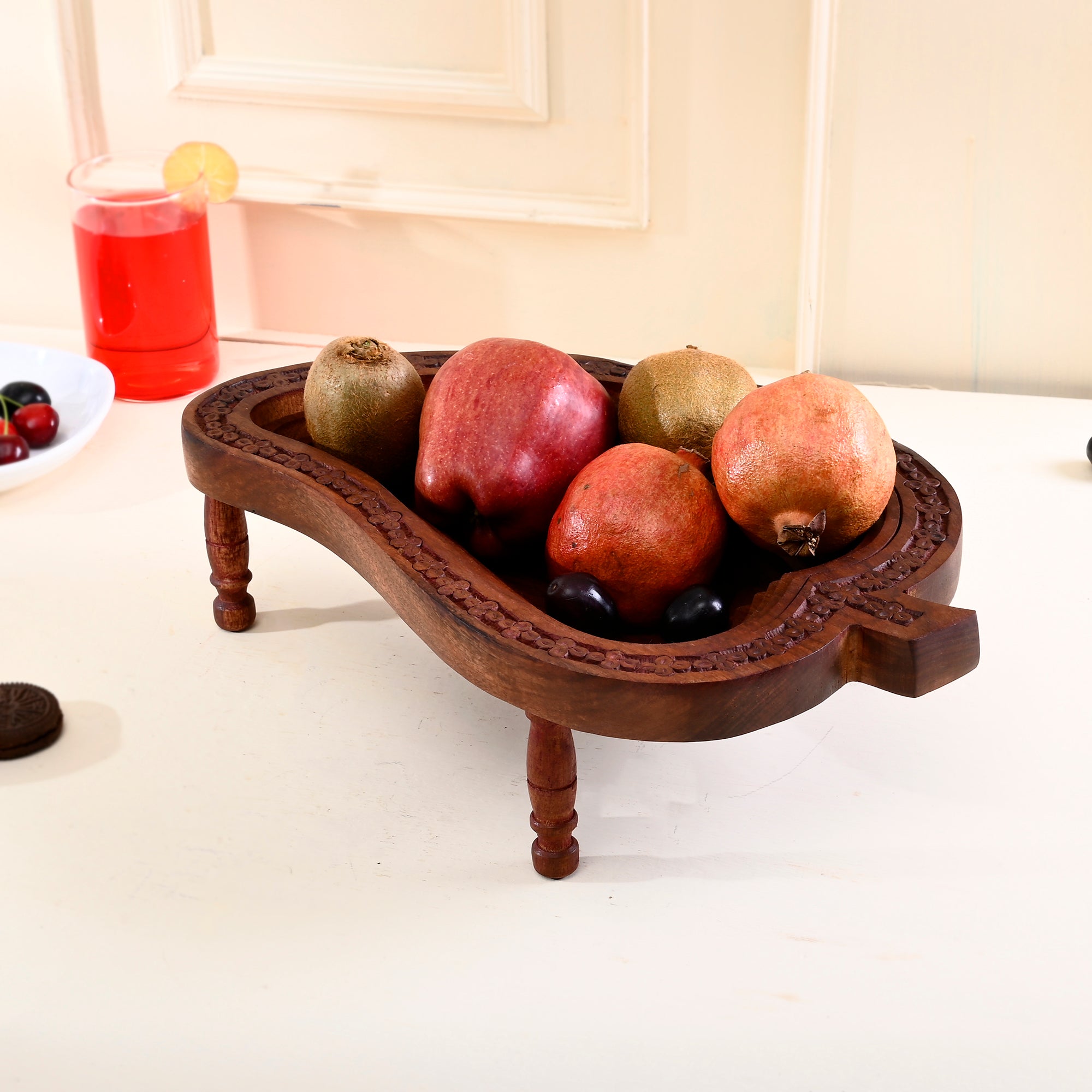 Wooden fruit tray with pomegranates and other fruits on a white surface.