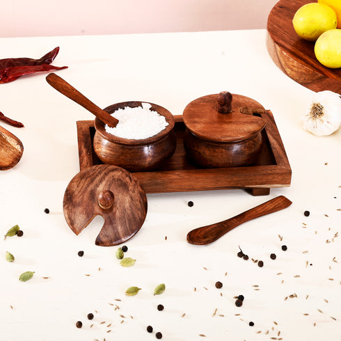Wooden spice containers with lids on a white surface with spices and herbs.