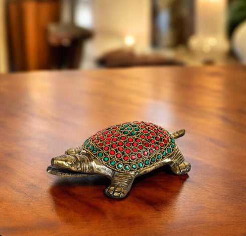 A brass tortoise figurine with a decorative red and green pattern on its back, displayed on a wooden surface.