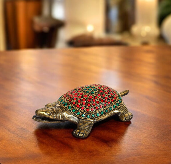 A brass tortoise figurine with a decorative red and green pattern on its back, displayed on a wooden surface.