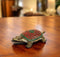 A brass tortoise figurine with a decorative red and green pattern on its back, displayed on a wooden surface.