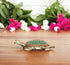 A brass tortoise figurine with a decorative red and green pattern on its back, displayed on a wooden surface.