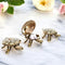 A set of three brass tortoise figurines with a secret wish compartment, placed on a marble surface with flowers in the background.