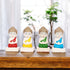 A set of four colorful mini Buddha statues, each with a different color, placed on a wooden surface with a plant in the background.