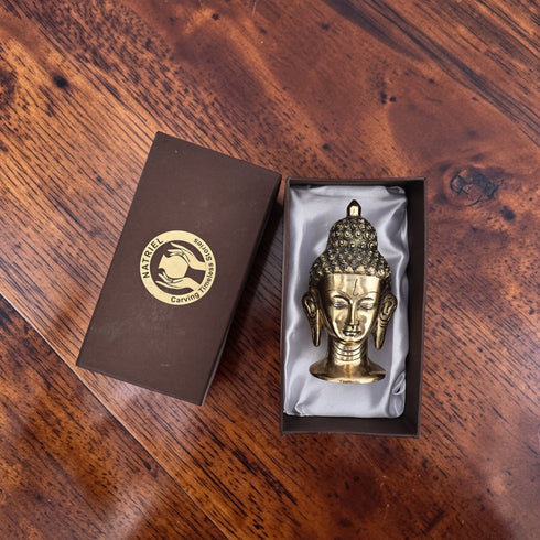 Gold Buddha statue in a box on a wooden surface with 'Nafplio' branding.