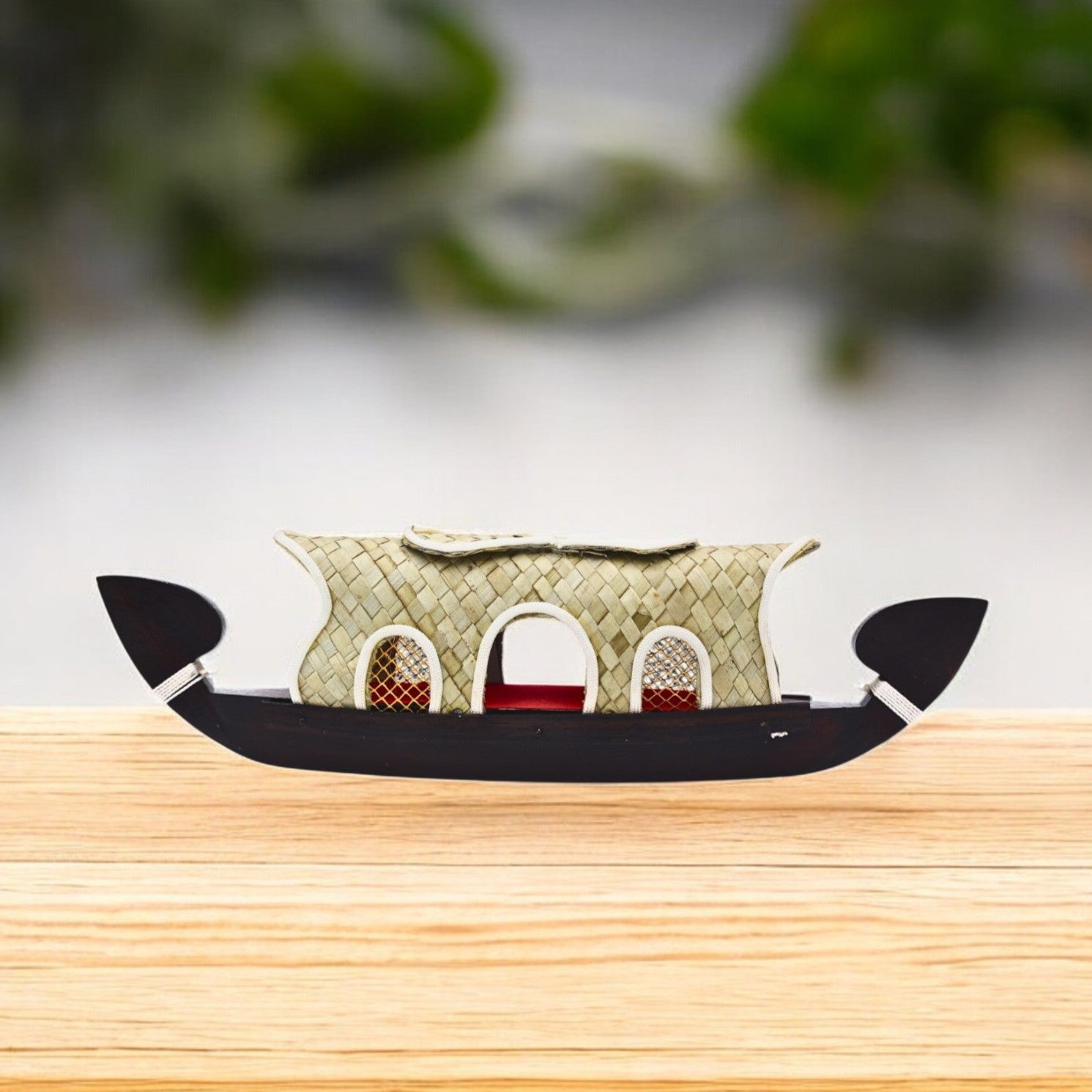 A miniature model of a wooden kettuvallam houseboat with a palm leaf canopy on top, displayed on a wooden surface.