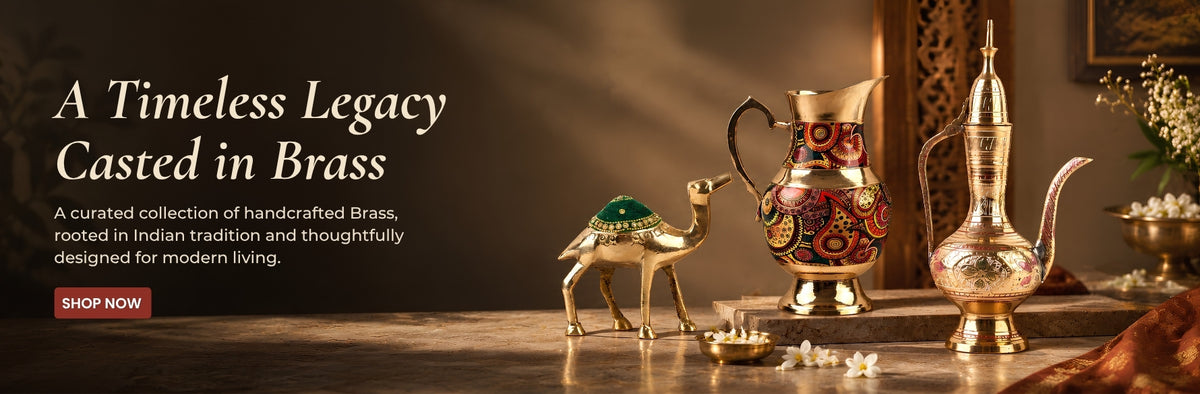 A styled product display featuring traditional brass and brass-finished home decor items on a wooden table, including a decorative camel figurine, a patterned pitcher, a tall ornate pitcher, and a small bowl, with promotional text on the left.