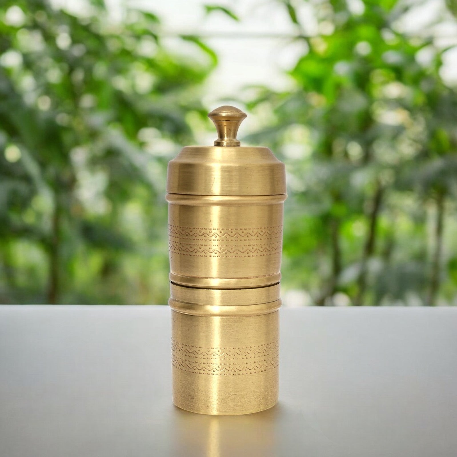 Brass grinder on a white surface with a blurred green background
