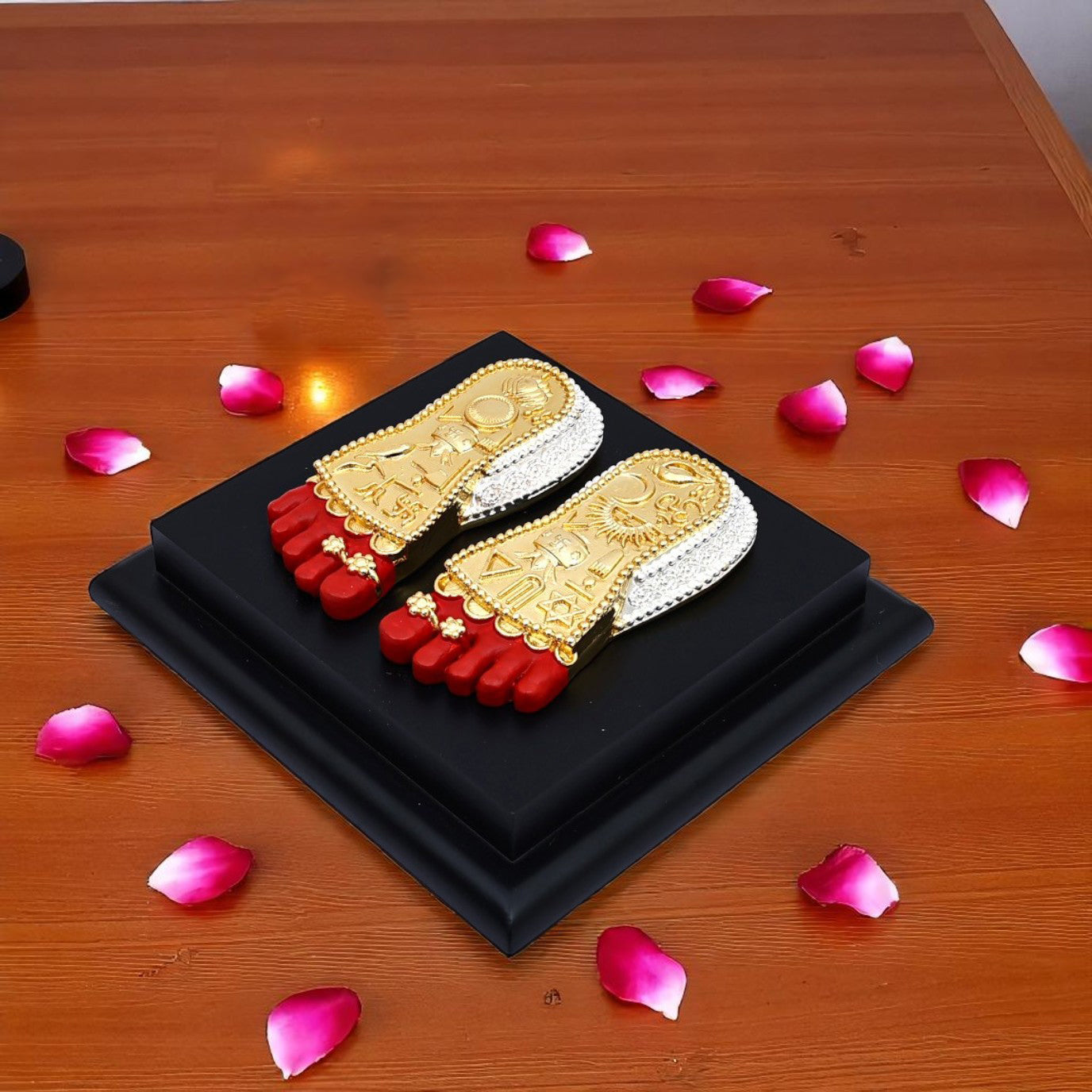 Decorative toe sandals with gold and red design on a black box, surrounded by pink petals on a wooden surface.