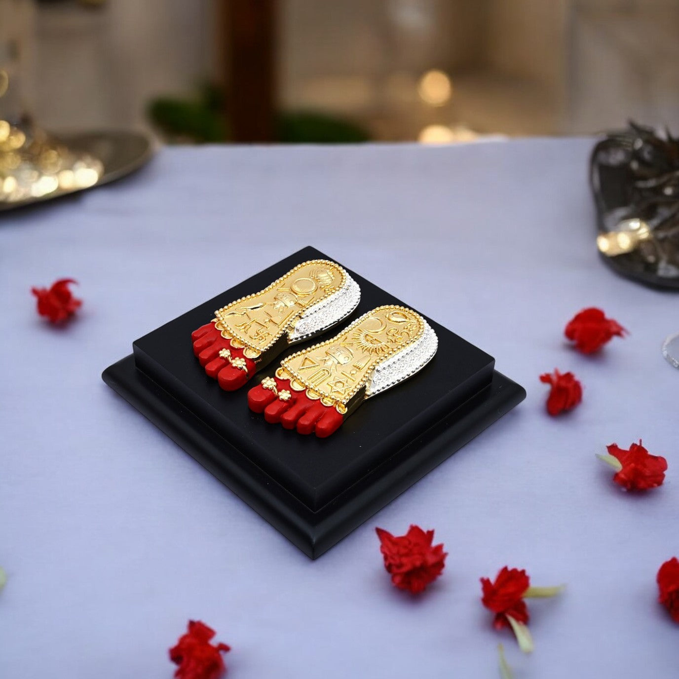 Gold and red toe rings on a black display box with red flowers around on a white surface.
