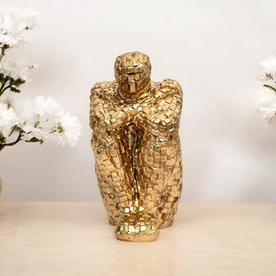 Gold mosaic sculpture on a neutral background with white flowers