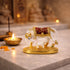 Decorative statue of a cow and calf with gold accents on a marble surface, with a lit candle in the background.