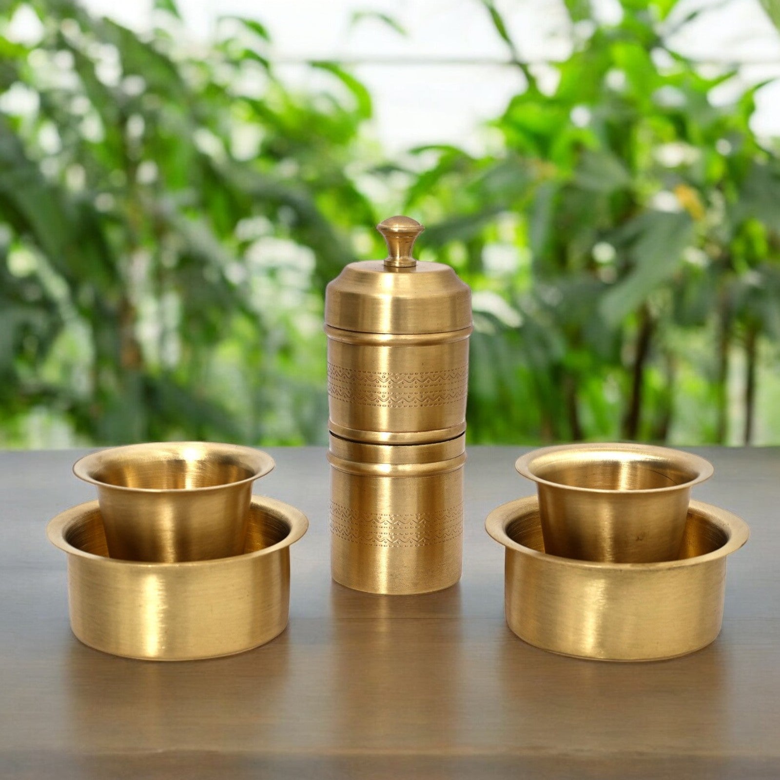 Set of three brass containers on a reflective surface with a blurred green outdoor background