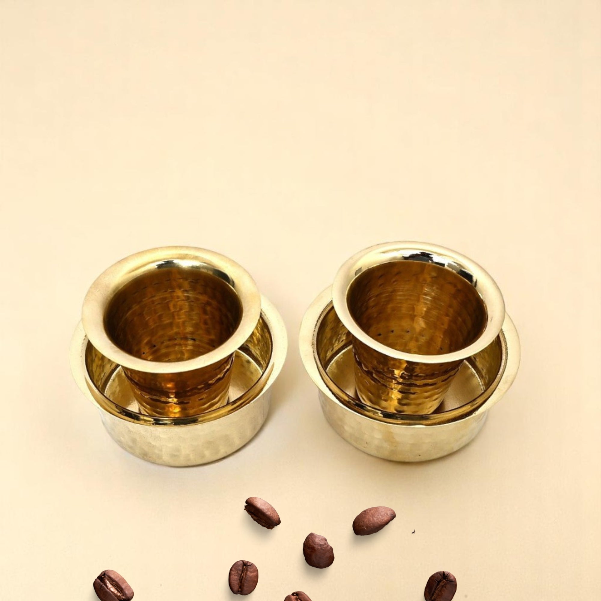 Two gold metal cups with coffee beans on a beige background